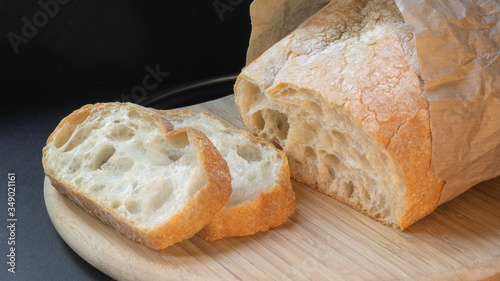 Beautiful bread closeup made from wheat flour on a wooden board on a black background in a paper bag. Sliced slices and half bread.