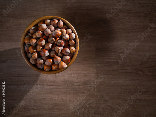 Picture of a bowl full of hazelnuts on the brown wooden table.