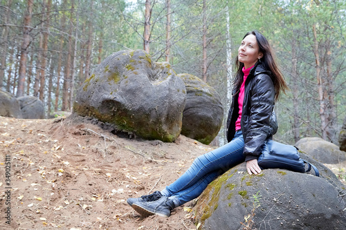 Beautiful young woman sitting on the big stone in the forest with sprice in autumn photo