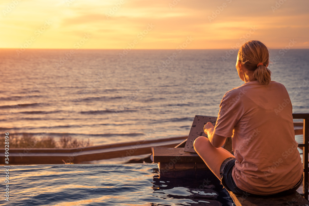 Fototapeta premium Young pensive woman looking at horizon with hope during travel vacation in warm orange colors at sunset over sea