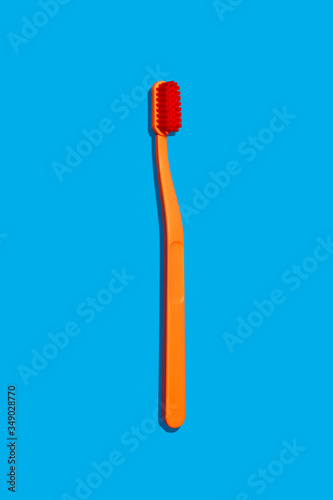 Modern Monochromatic Orange Hero Toothbrush Laying on Blue Background Isolated (ID: 349028770)