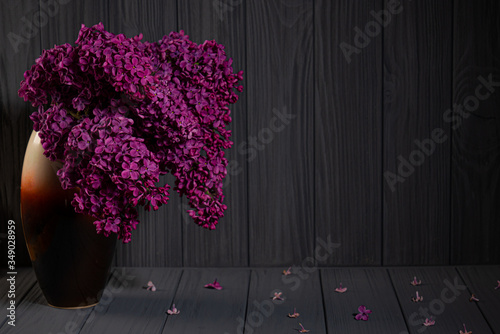 Bouquet of pink lilac flovers in vase on wooden table with fallen petals