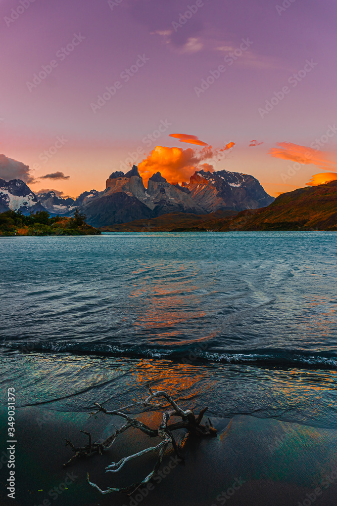 Vertical photo of a lake with some rocky snowy peaks of a mountain with the sun coming out behind