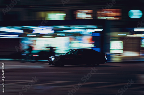 Panning shot of a black sedan on road at a night in the middle of city