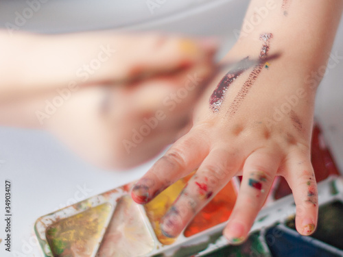 Kid is paintning on his hands. Colorful paints. photo