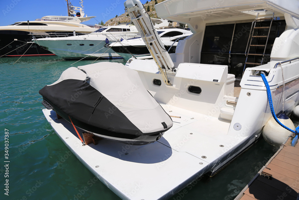Fototapeta premium A rubber, latex high-speed motor boat stands on a large two-deck yacht in a sheathed form, secured with cables. The boat is closed from rain and wind, waiting for good weather and tourist season. Conc