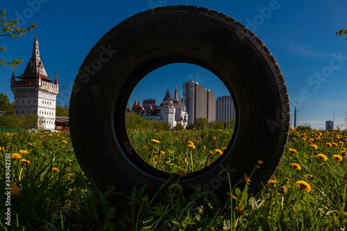 An old car tire stands in a meadow. Through it you can see the building of a fairytale castle