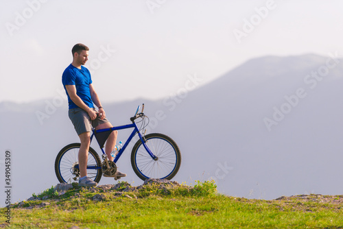 Fit mountain biker riding his bike through green grass on top of a mountain.
