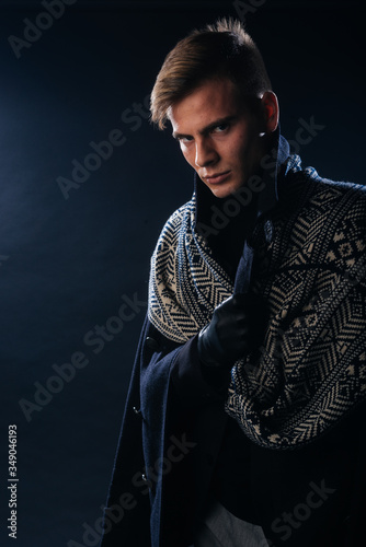 Portrait of a handsome with sharp jawline young man wearing a scarf while posing inside a studio on a black background..