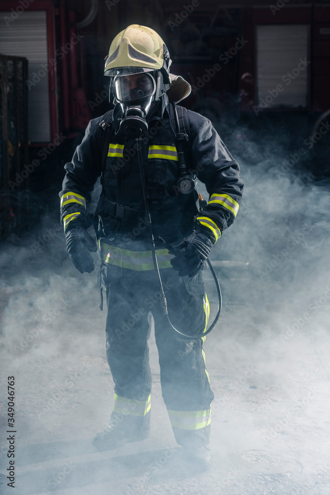 Obraz premium Portrait of a fireman wearing firefighter turnouts and helmet. Dark background with smoke and blue light.