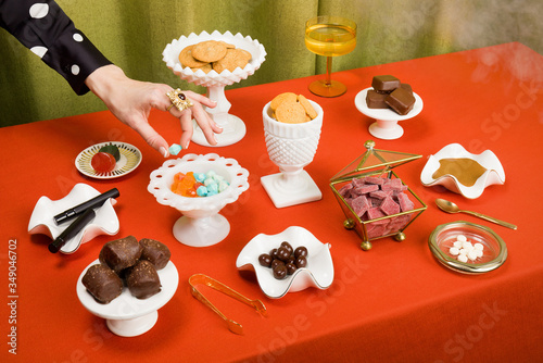 Still Life Spread of Cannabis Edibles in Milk Glass on Red Tablecloth with Hand Horizontal (ID: 349046702)