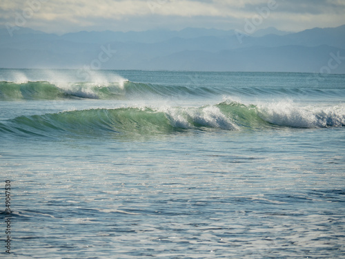 Sticker crashing waves on New Zealand beach with hazy mountains on horizon