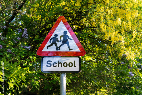 school sign in London, UK.  Warning to slow down road sign with trees in the background