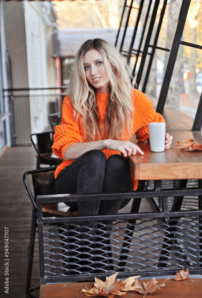 Beautiful woman in orange sweater drinks coffee outdoors 