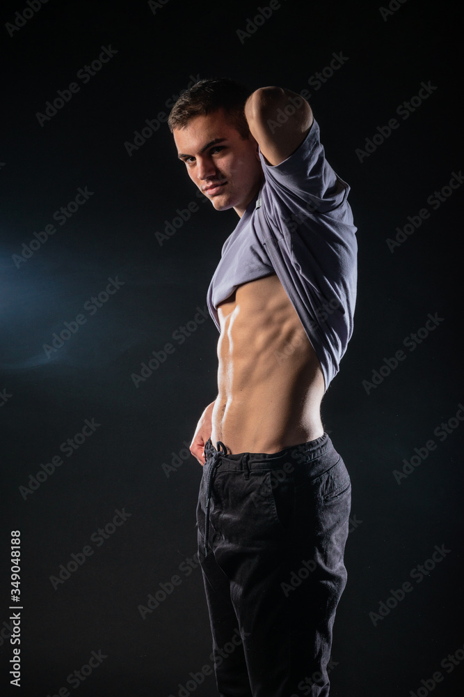 Sexy male model showing his abs while posing in a studio on dark backgorund. Sexy male model showing his abs while posing in a studio on dark backgorund.