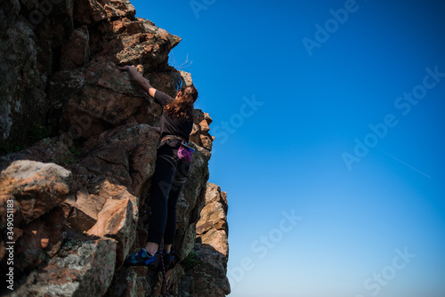 A woman rock climbing looking up in the sky