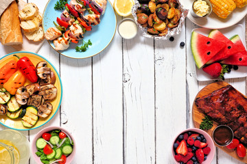 Summer BBQ or picnic food frame. Variety of grilled meats, vegetables, fruits, salad and potatoes. Above view over a white wood background. Copy space.