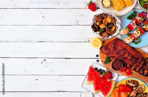 Summer BBQ or picnic food side border. Selection of grilled meat, vegetables, fruits and potatoes. Top down view over a white wood background. Copy space.