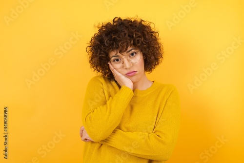 Very bored adult businesswoman holding hand on cheek while support it with another crossed hand, looking tired and sick, over white background. © Roquillo