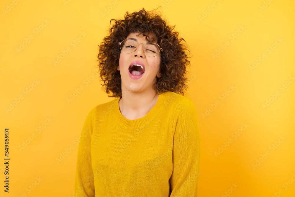 Beautiful woman with curly short hair wearing casual yellow sweater over yellow background winking looking at the camera with sexy expression, cheerful and happy face. Beautiful woman with curly short hair wearing casual yellow sweater over yellow background winking looking at the camera with sexy expression, cheerful and happy face.