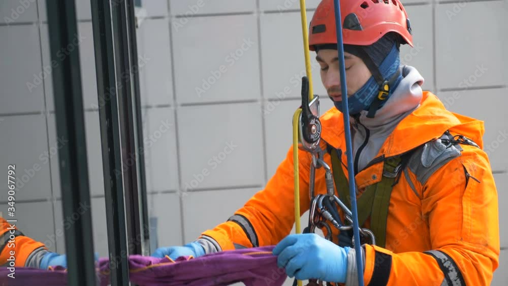 professional industrial climber in an orange helmet wipes the remains with special rag and slides down rope with trigger, slow motion professional industrial climber in an orange helmet wipes the remains with special rag and slides down rope with trigger, slow motion