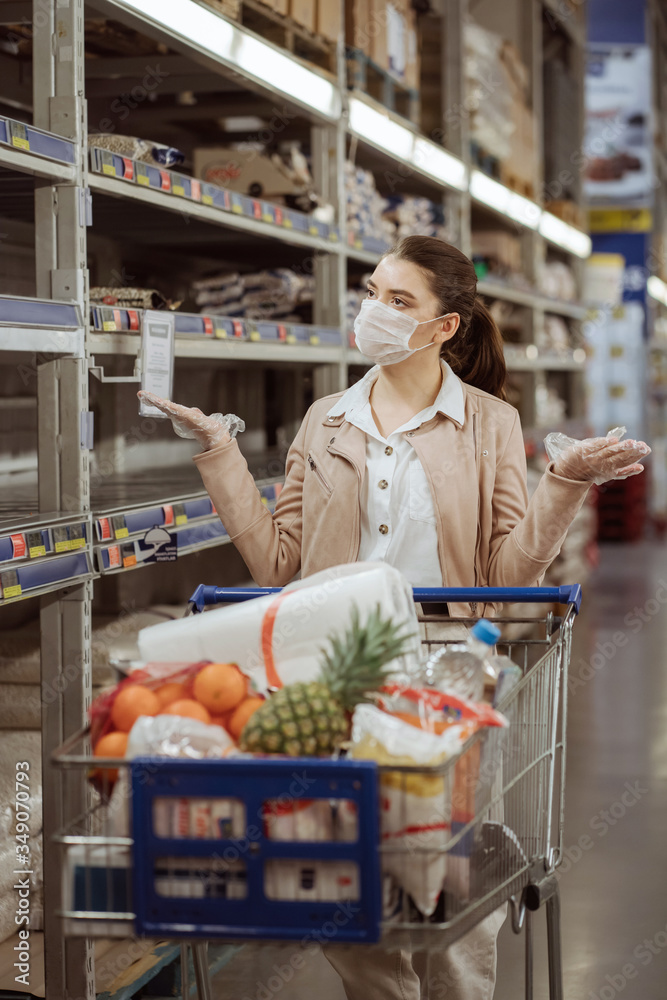 woman in gloves and a medical mask in a supermarket is outraged by the lack of food on the shelf.