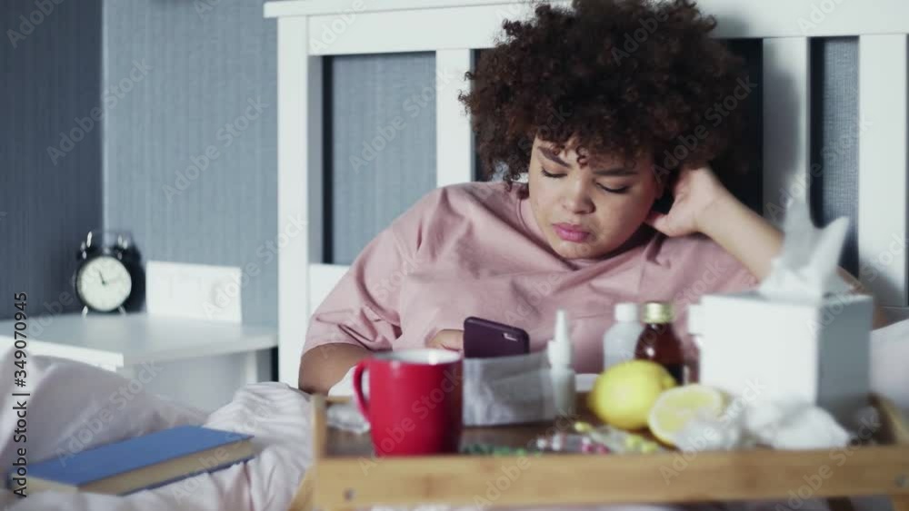 Sick Young african american girl using phone in bed at home Sick Young african american girl using phone in bed at home