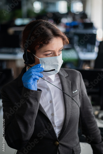 Female call center operator talking to a customer. Woman in mask and gloves at the workplace in the office. Social distance and safety measures to prevent infection.