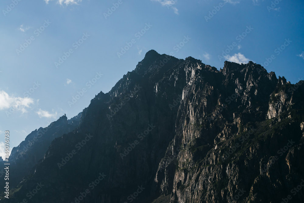 Awesome view to pointy peak of dark rock in clear blue sky. Minimalist alpine landscape with big black mountain. Atmospheric highland scenery with huge rocky pinnacle top. Mysterious crag in backlight