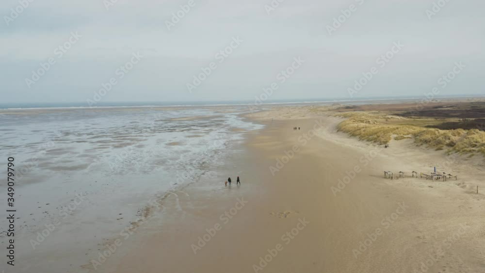 A group of people walking on an empty beach on frisian island Borkum next to dunes and wadden sea of the north sea - Drone aerial circling shot A group of people walking on an empty beach on frisian island Borkum next to dunes and wadden sea of the north sea - Drone aerial circling shot