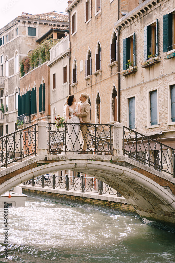 Italy wedding in Venice. The bride and groom are standing on a stone bridge over a narrow Venetian canal. Newlyweds walk around the city taking pictures on the street.