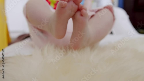 Baby kicks her legs and wiggles her tiny toes while lying on a sheep skin mat photo