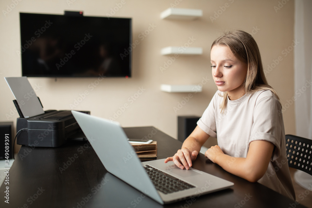 Cute pensive girl does work from home on a remote computer at a desk with a notebook and a telephone on the table during quarantine and pandemic. Cute pensive girl does work from home on a remote computer at a desk with a notebook and a telephone on the table during quarantine and pandemic.