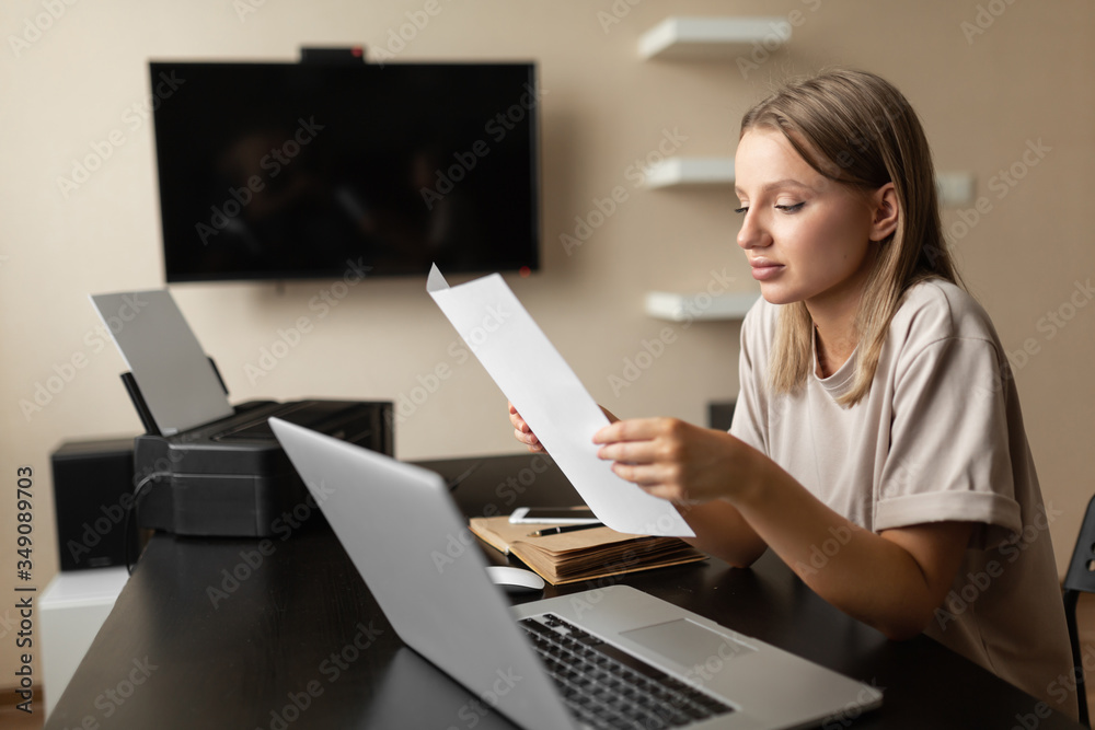 beautiful, lovely girl does work from home smiling and reading information on a sheet of paper sitting at a computer during quarantine. beautiful, lovely girl does work from home smiling and reading information on a sheet of paper sitting at a computer during quarantine.