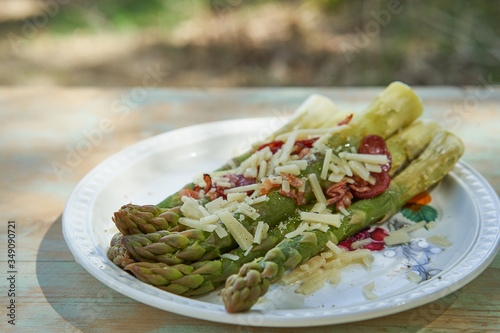 Boiled fresh green asparagus stalks with grated italian cheese and roasted spicy sausage and served on the vintage porcelain plate. Light and healthy seasonal spring dish, full of balanced nutritions.