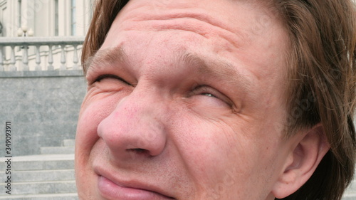 portrait of a white charismatic man looking at the sun and camera on city architecture background and squinting laughing slow motion close up video in 4K