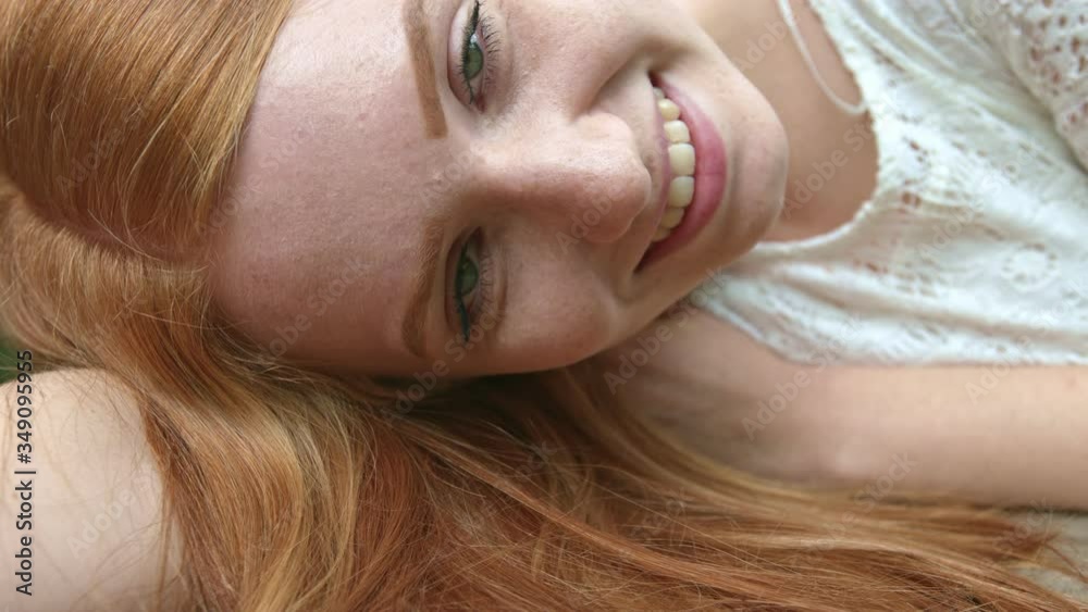 Close up portrait of young ginger hair green eyes female lying on her side. Looking straight into camera showing beautiful smile. Close up portrait of young ginger hair green eyes female lying on her side. Looking straight into camera showing beautiful smile.