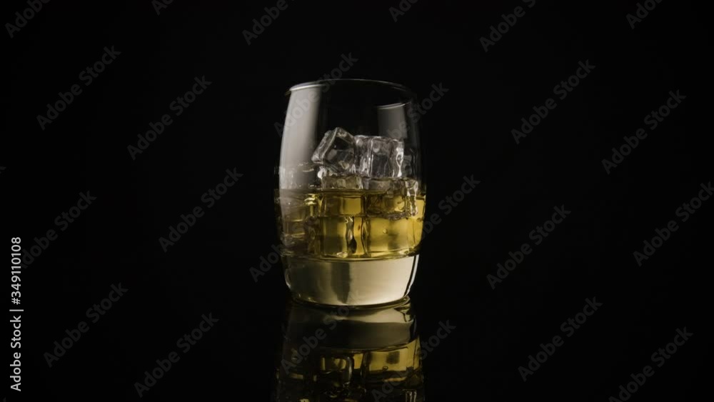 Slow push in on a glass tumbler containing whiskey and ice cubes on an infinite black background. Slow push in on a glass tumbler containing whiskey and ice cubes on an infinite black background.