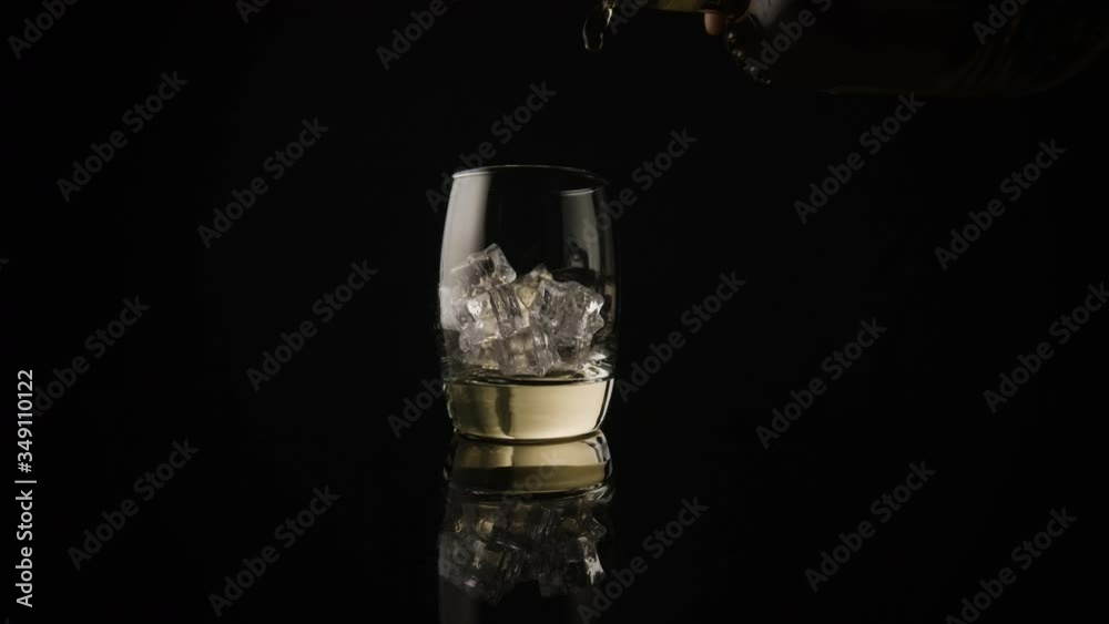 Pouring a whiskey on the rocks. Slow motion push in shot, isolated on black. Pouring a whiskey on the rocks. Slow motion push in shot, isolated on black.