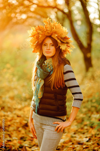 Close up portrait of a beautiful girl in a blue vest  stands against the backdrop of a fabulous autumn. On the head is a lush wreath with autumn leaves. Very tender model looking at the camera.