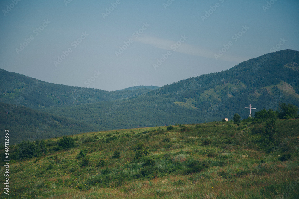 Obraz premium green mountains and a cross on the horizon. religious object to nature. Church building, ritual symbol, cemetery