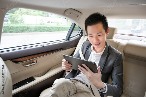 Handsome asian businessman working with tablet. Young executive manager Full concentration at work while sitting in the car. © komgritch