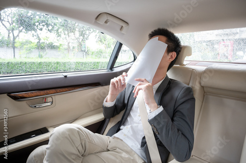 Stressed young asian businessman looking at Financial documents with expression Tired and worried while sitting on the back seat in the car.  many bad financial report. © komgritch