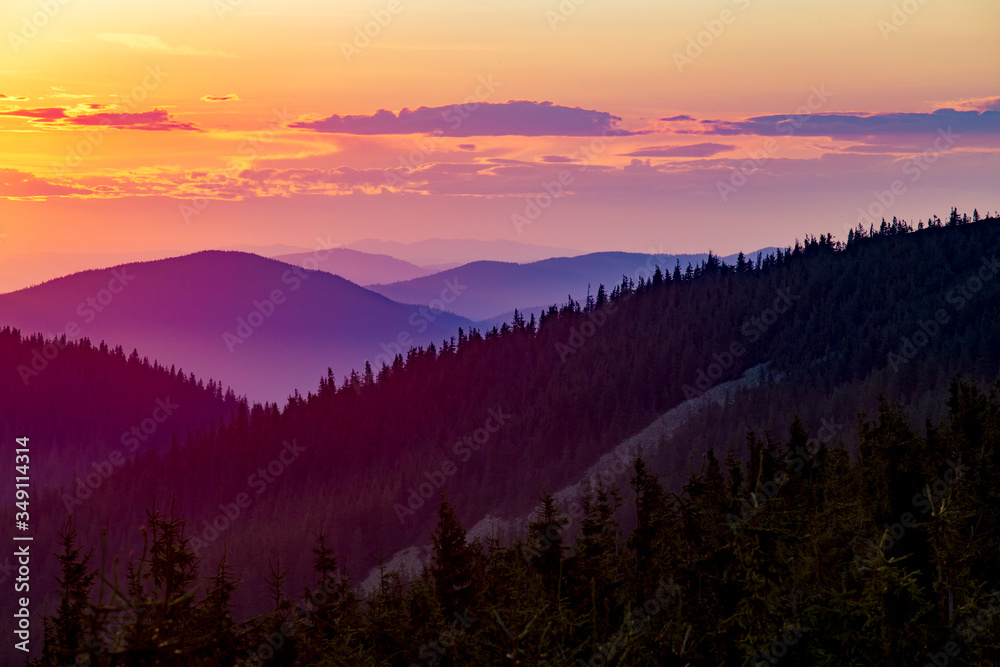 Sunset in the mountains. Mountain slopes and coniferous forest against the backdrop of mountain ranges and the sky with clouds at sunset