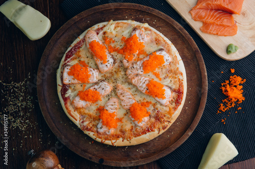 Salmon pizza topped with ebiko in a brown wooden plate