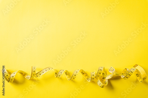 Measuring tape lying on a yellow background, simbol of diet, healthy eating and weight loss concept, with copy space for text.