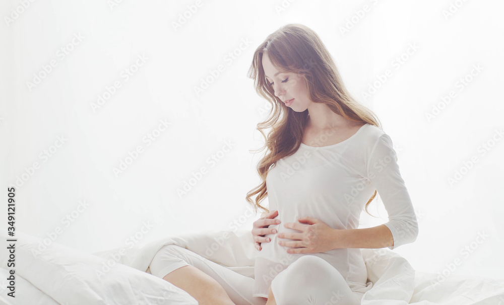 Happy pregnant woman touching her beautiful belly sitting in the bed. Pregnancy, motherhood, and expectation Happy pregnant woman touching her beautiful belly sitting in the bed. Pregnancy, motherhood, and expectation