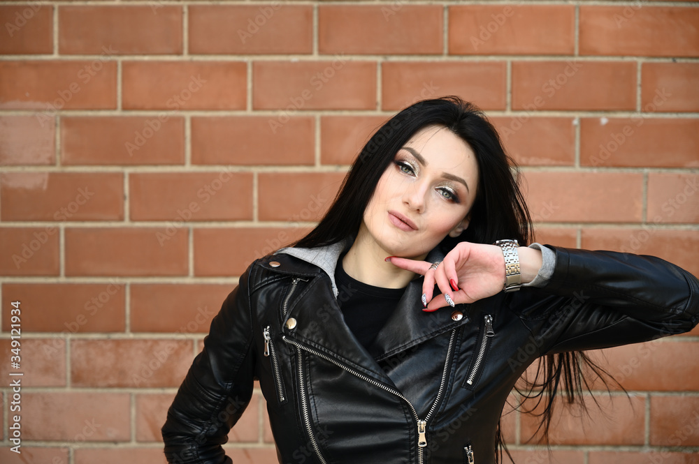 Model posing against the backdrop of a building wall. Close-up portrait in spring weather outdoors caucasian fashionable brunette girl in black jacket. Model posing against the backdrop of a building wall. Close-up portrait in spring weather outdoors caucasian fashionable brunette girl in black jacket.