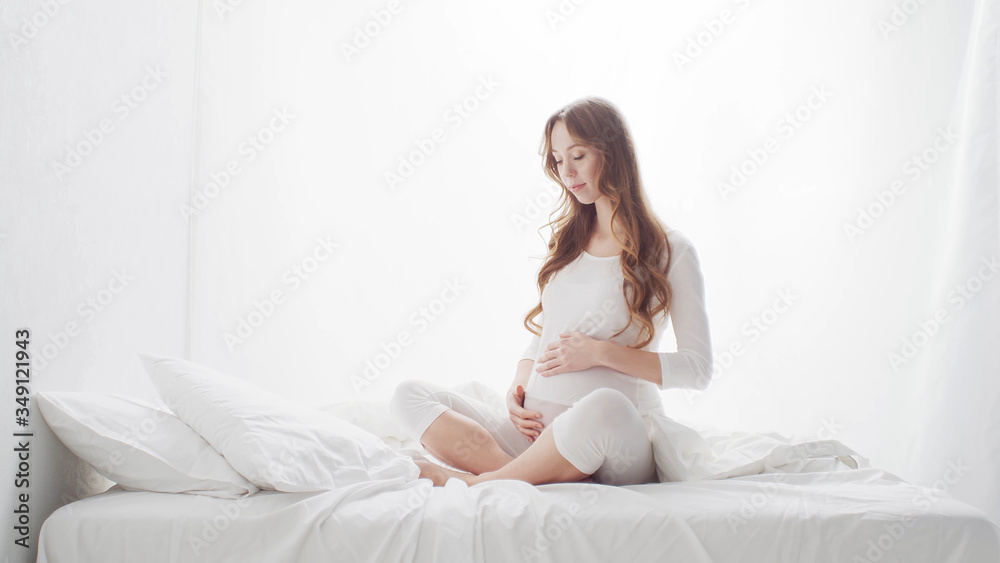 Happy pregnant woman touching her beautiful belly sitting in the bed. Pregnancy, motherhood, and expectation Happy pregnant woman touching her beautiful belly sitting in the bed. Pregnancy, motherhood, and expectation