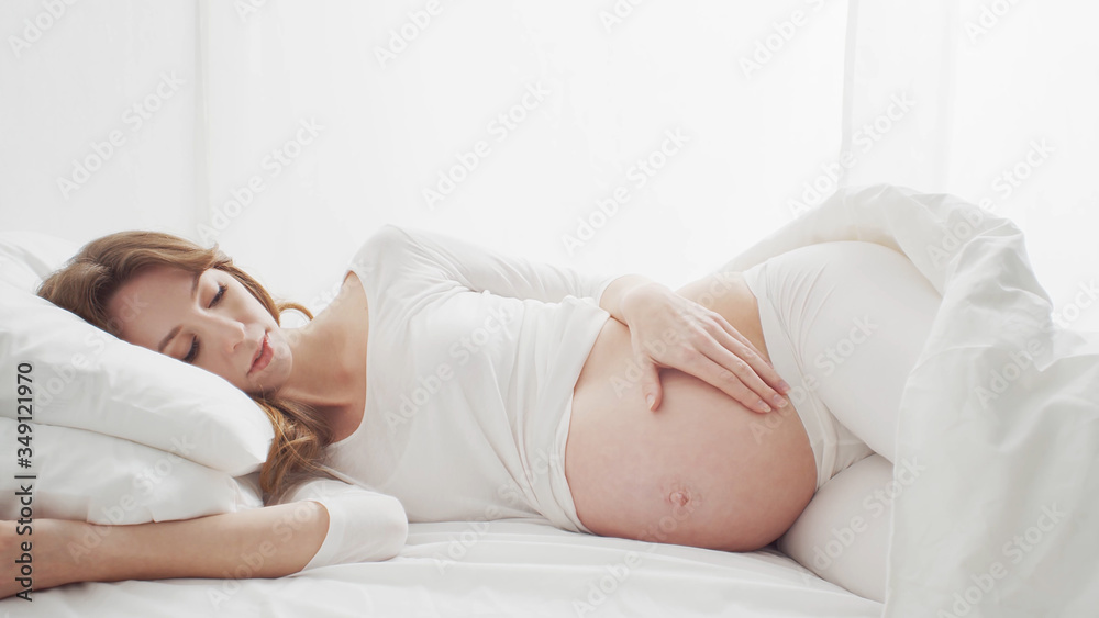 Happy pregnant woman touching her beautiful belly sitting in the bed. Pregnancy, motherhood, and expectation